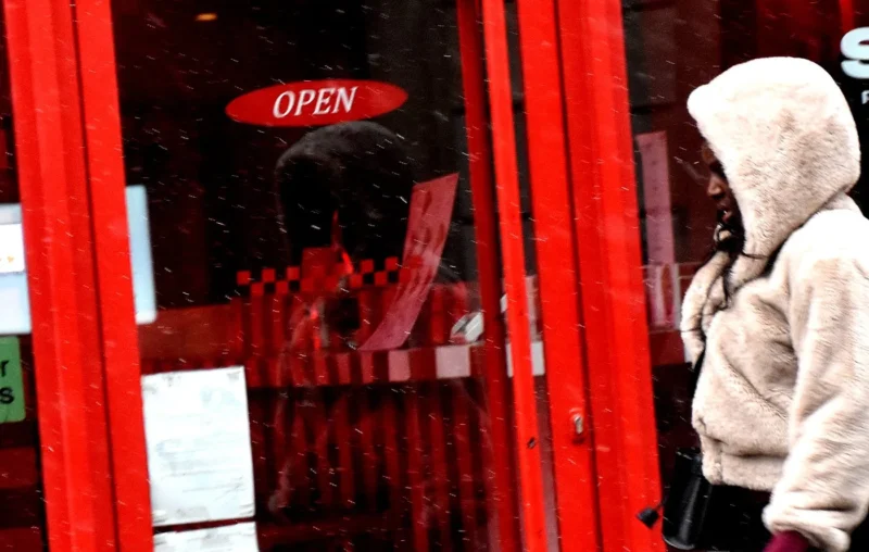 Franck T. · 05/01/2026 · 1400 x 889 Cette photographie montre un reflet dans une vitrine rouge avec un panneau "OPEN". Le sujet principal est flou, mais on distingue une silhouette vêtue d'une veste blanche et d'un bonnet. La composition joue sur les reflets et les contrastes entre intérieur et extérieur. Le cadrage est serré, centré sur la vitrine et son reflet.Les couleurs dominantes sont le rouge vif et le blanc. La lumière semble naturelle, mais légèrement tamisée, créant une ambiance urbaine et légèrement mystérieuse. Le style est réaliste et spontané, évoquant une scène de rue banale mais captée avec un angle original.