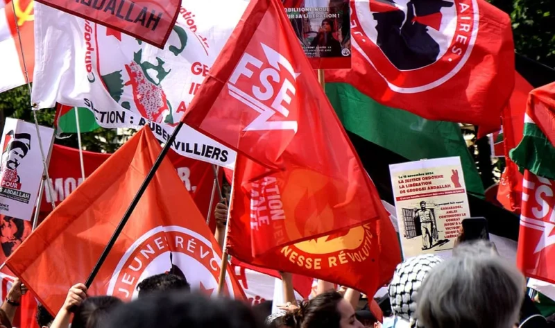 Franck T. · 14/06/2025 · 1000 x 591 Cette photographie montre une manifestation avec des drapeaux et bannières comme sujets principaux. Les couleurs dominantes sont le rouge, le blanc et le vert, avec des inscriptions en français et des logos syndicaux (comme CES et FO).La composition est dynamique, avec des éléments superposés et des visages partiellement visibles. Le cadrage est serré, mettant en avant les symboles et messages politiques. La lumière semble naturelle, bien répartie, créant une ambiance claire et énergique. L'ensemble dégage une impression de mobilisation et de protestation collective.