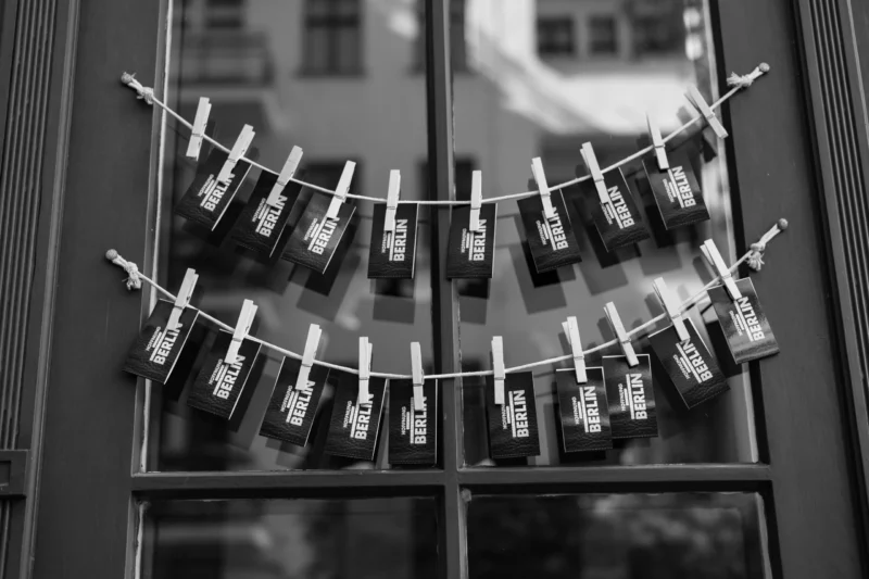 Claude · 6000 x 4000 Cette photographie en noir et blanc montre comme sujet principal une corde à linge avec plusieurs petits sachets suspendus, probablement des sachets de thé ou des épices.La composition est symétrique et horizontale, avec les sachets alignés de manière régulière. Le cadrage est serré sur la corde, encadrée par une fenêtre divisée en carreaux.La lumière est douce, créant des contrastes nets entre les ombres et les formes. Les couleurs dominantes sont les nuances de gris, renforçant une ambiance minimaliste et épurée. Le style est sobre et artistique, évoquant une touche vintage et intemporelle.