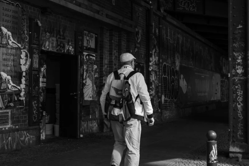 Claude · 6000 x 4000 Cette photographie en noir et blanc met en scène un homme en tenue militaire, marchant dans une ruelle urbaine. Le sujet principal est centré, avec une silhouette contrastée par l’ombre et la lumière.La composition utilise un cadrage serré sur le personnage, encadré par des murs couverts de graffitis. La lumière, basse et contrastée, accentue les textures et crée une ambiance dramatique. Les ombres allongées renforcent l’aspect mystérieux et sombre. Le style, réaliste et documentaire, évoque une atmosphère de tension et de solitude dans un environnement urbain dégradé.