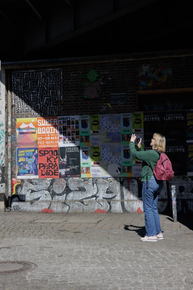 Claude · 3796 x 5694 Cette photographie montre une personne prenant une photo d’un mur tagué et coloré. Le sujet principal est ce mur recouvert de graffitis et d’affiches publicitaires. La composition est verticale, avec un cadrage serré sur le mur et la personne en bas à droite. La lumière est tamisée, ambiance nocturne ou peu éclairée. Les couleurs dominantes sont vives (bleu, rouge, jaune) contrastant avec les tons sombres de la nuit. Le style est urbain et spontané, évoquant une ambiance street art et créative.