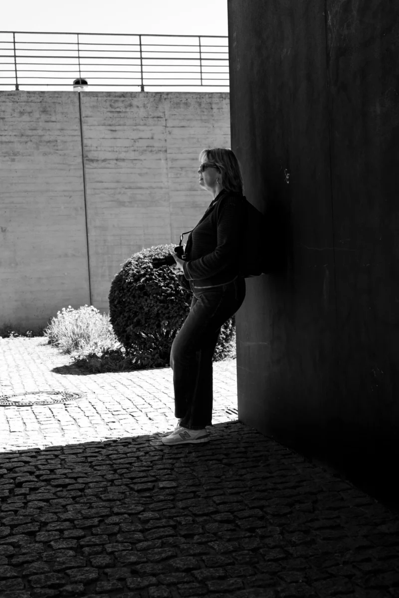 Claude · 3801 x 5701 Cette photographie en noir et blanc met en scène une personne comme sujet principal, vêtue d’un pantalon large et d’un chapeau, tenant un objet enroulé. La composition joue sur un cadrage serré et une perspective diagonale, guidant le regard vers l’ombre et la lumière contrastée. Le jeu d’ombres et de clarté, accentué par la lumière naturelle, crée un effet dramatique. Les tons dominants, du blanc au noir en passant par les gris, renforcent une ambiance à la fois mystérieuse et contemplative. Le style minimaliste et épuré évoque une esthétique documentaire ou artistique, soulignant la solitude et la simplicité.
