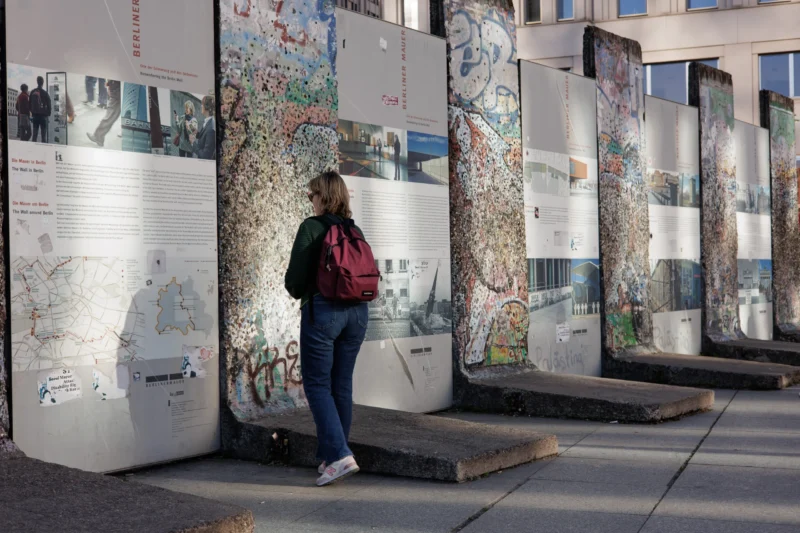 Claude · 5798 x 3865 Cette photographie montre une femme en mouvement, vêtue d’un manteau rouge, marchant devant une série de vitrines murales exposant des cartes et des dessins.La composition est dynamique, avec un cadrage serré sur la femme et les vitrines en arrière-plan. La lumière semble naturelle, probablement en journée, éclairant les éléments sans ombres marquées. Les couleurs dominantes sont les tons froids des vitrines et les couleurs vives des dessins, contrastant avec le rouge du manteau de la femme.L’ambiance est urbaine et artistique, évoquant une exposition publique ou un lieu culturel. Le style est réaliste et contemporain.