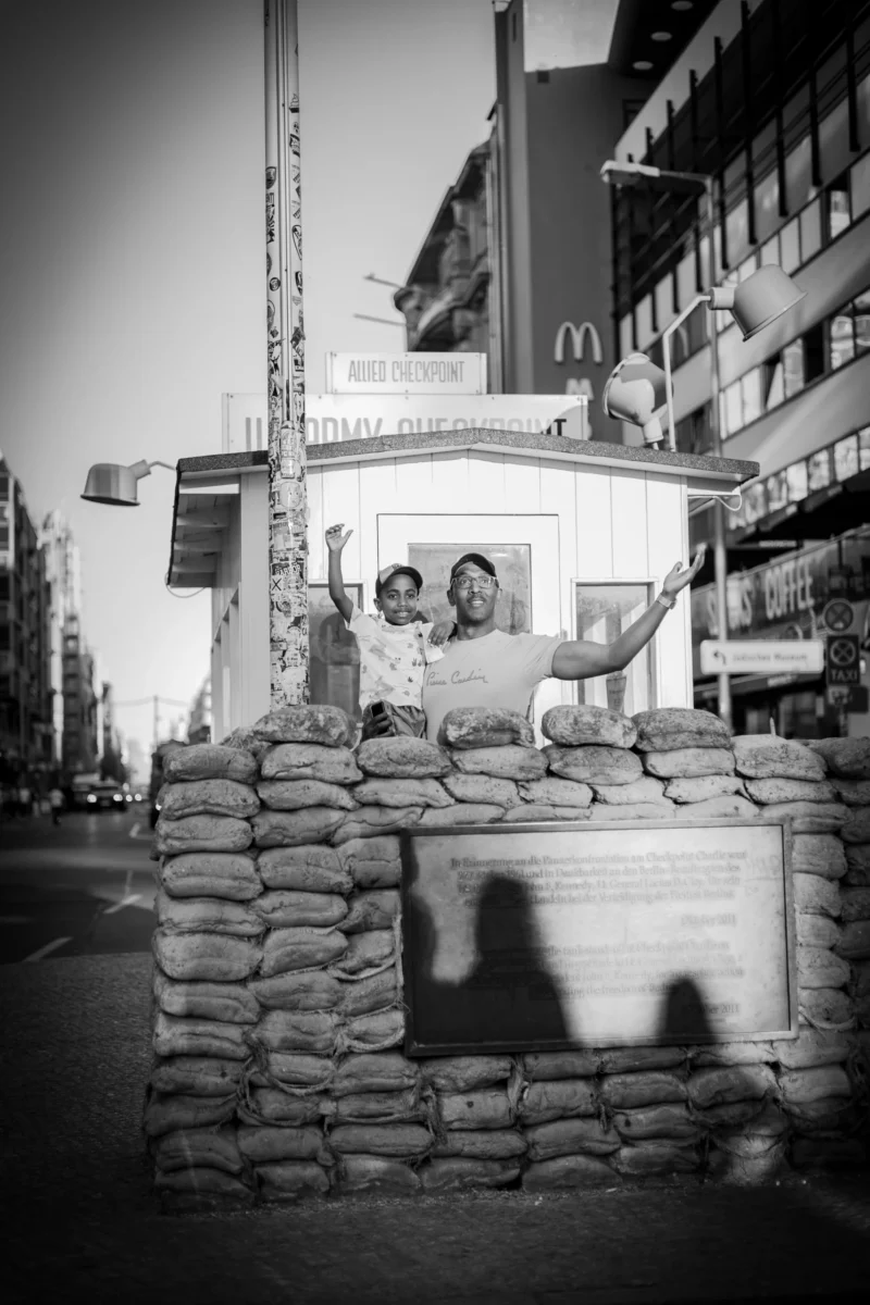 Claude · 3841 x 5762 Cette photographie en noir et blanc montre deux personnes assises sur un petit ponton de pierre, sujet principal. La composition met en avant un cadrage serré sur elles, avec un arrière-plan urbain flou incluant des bâtiments et des enseignes. La lumière est douce, créant des contrastes modérés et des ombres nettes. Le style est documentaire et intime, évoquant une ambiance calme et mélancolique. Les tons dominants sont les gris et noirs, renforçant une atmosphère nostalgique et contemplative.