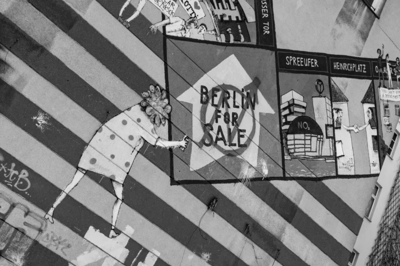 Claude · 6000 x 4000 Cette photographie en noir et blanc montre une affiche de rue avec le texte "BRADY'S SALE". Le sujet principal semble être une illustration de personnages et de bâtiments stylisés, évoquant un quartier animé.La composition est dynamique, avec des lignes horizontales et verticales contrastées. Le cadrage est serré sur l’affiche, intégrée dans un environnement urbain. La lumière est uniforme, sans ombres marquées, renforçant l’aspect graphique. Les couleurs dominantes sont les tons de gris, typiques d’une photo en noir et blanc.Le style est épuré et rétro, évoquant une ambiance vintage et artistique.