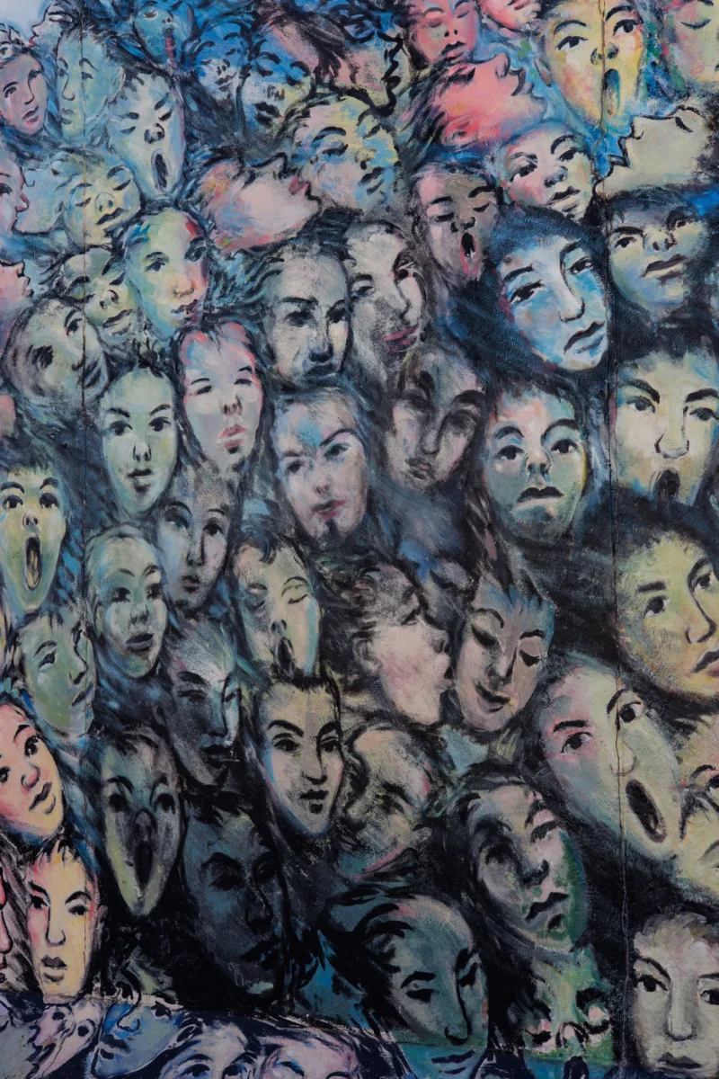 Claude · 4000 x 6000 Cette photographie représente une œuvre artistique murale composée de multiples visages stylisés et superposés. Le sujet principal est l'expression collective et variée des émotions humaines.La composition est dense et dynamique, avec un cadrage serré qui met en valeur les détails des traits. Les couleurs dominantes sont douces et pastel, avec des touches de bleu, violet et rose, créant une ambiance à la fois mélancolique et onirique. Le style est abstrait et expressionniste, évoquant une atmosphère à la fois intime et universelle. La lumière semble uniforme, sans ombres marquées, renforçant l'harmonie des tons.