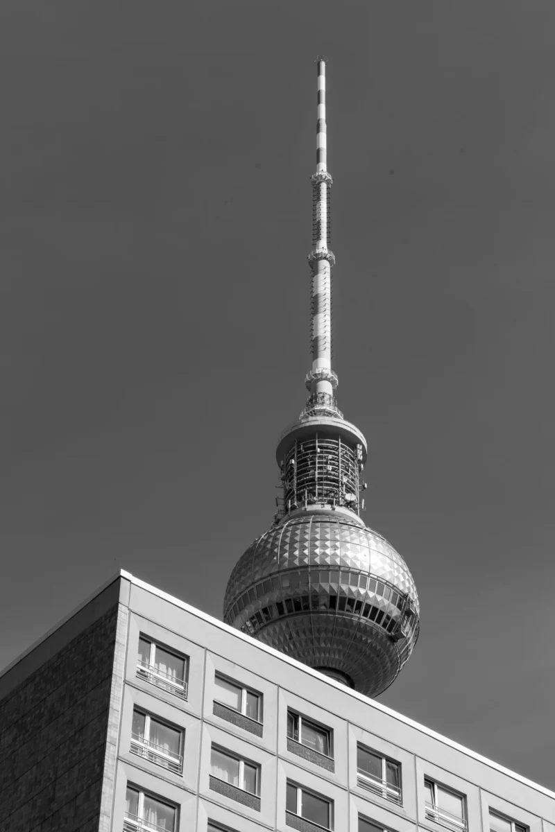 Claude · 3772 x 5658 Cette photographie met en scène une tour emblématique, probablement la tour de la télévision de Berlin. Le sujet principal est son dôme métallique et sa flèche élancée. La composition est verticale, avec un cadrage serré sur la structure, isolant la tour du reste de l’environnement.La lumière est naturelle, contrastée, créant des ombres marquées. En noir et blanc, les tons dominants varient du blanc pur aux gris profonds, accentuant les textures et les détails architecturaux. Le style est épuré et documentaire, évoquant une ambiance à la fois moderne et intemporelle.