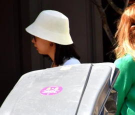 Franck T. · 09/05/2026 · 1400 x 764 Cette photographie met en scène deux femmes de dos. La personne à gauche porte un chapeau blanc et une veste claire, tandis que celle à droite, vêtue d’un pull vert et de lunettes, semble observer quelque chose. Le sujet principal est la femme en vert, dont le visage est partiellement visible.La composition est simple, avec un cadrage serré sur les deux femmes. La lumière semble naturelle, probablement en extérieur, avec des ombres douces. Les couleurs dominantes sont le vert du pull, le blanc du chapeau et les tons neutres des vêtements. L’ambiance est discrète et quotidienne, évoquant une scène urbaine ou un moment de pause.
