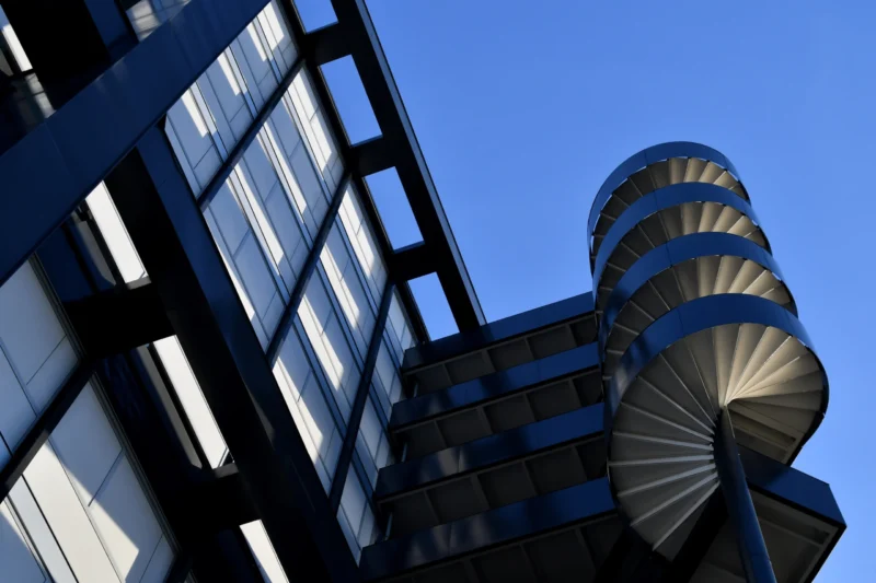 Vincent · 17/01/2026 · 5400 x 3600 Cette photographie met en scène un immeuble moderne avec une tour hélicoïdale en spirale. Le sujet principal est cette structure architecturale futuriste.La composition joue sur les lignes verticales et la perspective ascendante, renforcée par le cadrage serré. La lumière, naturelle et vive, éclaire les surfaces, créant des contrastes nets entre ombres et lumières.Les couleurs dominantes sont les tons gris métalliques et bleus du ciel. Le style est épuré et contemporain, évoquant une ambiance urbaine et technologique, presque minimaliste.