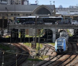 Vincent · 16/05/2026 · 5568 x 3712 Cette photographie montre un train moderne en mouvement sur des voies ferrées, sujet principal. La composition inclut une gare avec des bâtiments et des voies multiples, ainsi que des véhicules en arrière-plan.Le cadrage est large, capturant une vue aérienne partielle. La lumière semble naturelle, avec des tons clairs mais sans éclat excessif. Les couleurs dominantes sont les teintes grises des infrastructures, bleues du train, et quelques touches de vert et brun pour les espaces extérieurs.Le style est documentaire et réaliste, évoquant une ambiance industrielle et urbaine, dynamique et fonctionnelle.
