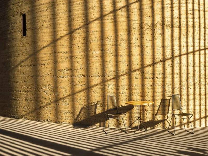 Thierry · 30/04/2026 · 3840 x 2560 Cette photographie capture des **chaises et une table** disposées sur une terrasse en bois, vues à travers des **barreaux métalliques**. Le **sujet principal** est l’ombre projetée et la lumière filtrée, créant un jeu graphique entre clarté et obscurité.La **composition** est épurée, avec un **cadrage serré** mettant en valeur les motifs géométriques. La **lumière**, douce et rasante, accentue les contrastes et les textures. Les **couleurs dominantes** sont des tons chauds (beige, brun) et des ombres dorées.Le style est **minimaliste et artistique**, évoquant une **ambiance calme et contemplative**, presque abstraite.