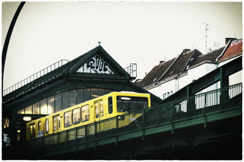 Thierry · 30/04/2026 · 3840 x 2560 Cette photographie met en scène un tramway jaune comme sujet principal, en mouvement sur une voie surélevée. La composition est dynamique, avec une perspective légèrement basse, encadrée par les structures métalliques et les bâtiments en arrière-plan.Le cadrage est serré, mettant l’accent sur le tram et son environnement immédiat. La lumière est tamisée, créant une ambiance sobre et légèrement nostalgique. Les couleurs dominantes sont les tons froids (gris, vert) contrastant avec le jaune vif du tramway. Le style évoque un réalisme teinté de mélancolie, renforcé par le flou et la patine sépia de l’image.