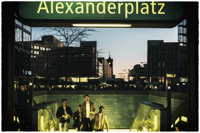Thierry · 30/04/2026 · 3840 x 2560 Cette photographie montre le **Alexanderplatz** à Berlin. Le **sujet principal** est un groupe de personnes assises sur un banc, en contrebas d’un passage piéton éclairé.La **composition** est équilibrée, avec un cadrage serré sur les personnages et un arrière-plan urbain. La **lumière** est artificielle, contrastée, mettant en valeur les néons et les contours des bâtiments. Les **couleurs dominantes** sont des teintes froides (bleus, gris) avec des éclats de vert et de jaune.Le **style** est réaliste et documentaire, évoquant une ambiance **urbaine et nocturne**, à la fois animée et mélancolique.