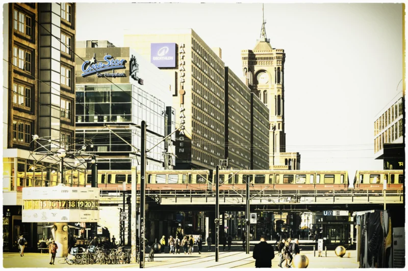 Thierry · 01/05/2026 · 3840 x 2560 Cette photographie montre une scène urbaine animée avec un tramway comme sujet principal. La composition met en valeur une intersection de bâtiments variés, dont un immeuble emblématique en arrière-plan. Le cadrage est large, capturant une vue dynamique de la rue et des passants.La lumière, douce et légèrement sépia, évoque une ambiance rétro. Les couleurs dominantes sont les tons neutres et grisés, avec des touches de bleu et de rouge sur les enseignes. Le style, légèrement vintage, rappelle les photographies anciennes. L’ambiance est à la fois mouvementée et nostalgique, reflétant une ville en pleine activité.