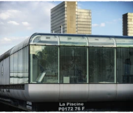 Thierry · 07/05/2026 · 3840 x 2560 Cette photographie met en scène un train moderne, sujet principal, avec une structure métallique et des vitres transparentes. La composition est horizontale, centrée sur le train en mouvement devant un arrière-plan urbain.Le cadrage est serré sur la partie avant du train, avec des bâtiments en arrière-plan. La lumière est naturelle, douce, avec des ombres peu marquées, suggérant un jour légèrement nuageux. Les couleurs dominantes sont les gris métalliques, les verts des arbres et les tons froids des bâtiments.Le style est réaliste et photographique, avec une ambiance dynamique et contemporaine, évoquant la modernité et l'efficacité.