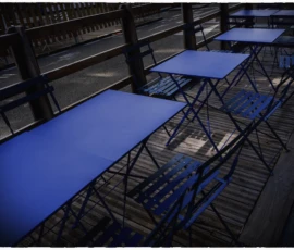 Thierry · 16/05/2026 · 3840 x 2560 Cette photographie montre des tables recouvertes de bâches bleues dans un espace industriel ou en rénovation. Le sujet principal est l'alignement des tables sous une structure métallique.La composition est géométrique et symétrique, avec un cadrage en plongée. La lumière, tamisée et artificielle, crée des contrastes nets entre ombres et surfaces éclairées. Les couleurs dominantes sont le bleu des bâches et les tons gris métalliques de la structure.Le style est épuré et minimaliste, évoquant une ambiance froide et industrielle, presque aseptisée.