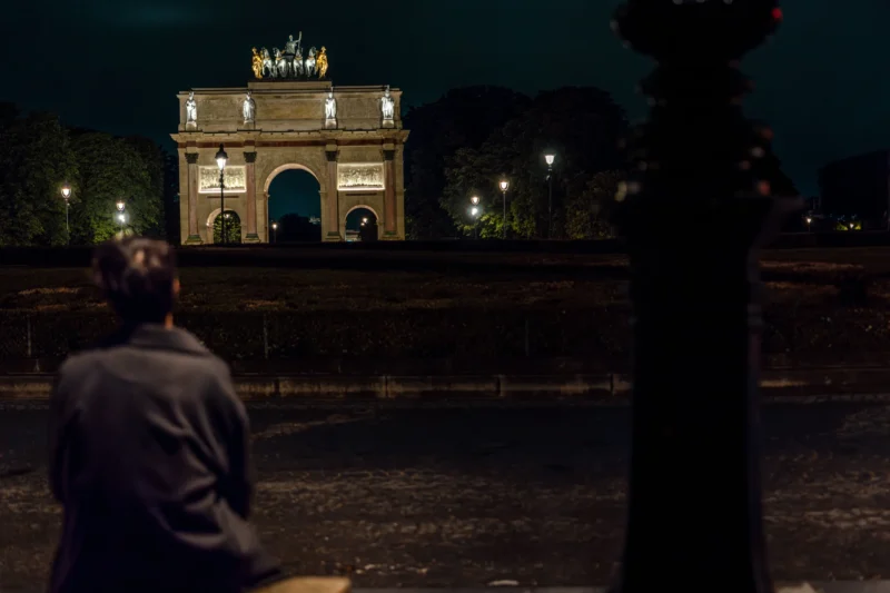 Marc L. · 17/05/2026 · 9504 x 6336 Cette photographie montre un homme assis dos à la caméra, observant un monument architectural imposant, probablement une porte triomphale, éclairée la nuit. La composition joue sur le contraste entre l’ombre du premier plan et la lumière dorée du monument. Le cadrage est serré sur l’homme, avec une profondeur de champ qui met en valeur les détails de l’édifice en arrière-plan.Les couleurs dominantes sont les tons sombres et les éclairages chauds. Le style est cinématographique, avec une ambiance nocturne mystérieuse et contemplative, renforcée par les jeux d’ombres et de lumières.