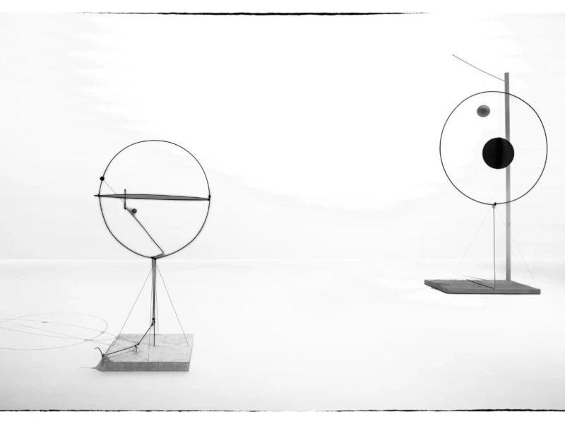 Thierry · 23/05/2026 · 3840 x 2560 Deux sculptures mécaniques circulaires avec des éléments mobiles posées sur des socles, en noir et blanc, ambiance
