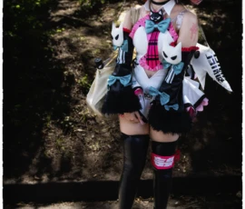 Thierry · 24/05/2026 · 2560 x 3840 Cette photographie met en scène une personne vêtue d’un cosplay coloré et fantaisiste, inspiré d’un personnage stylisé. Le sujet principal est au centre, avec une tenue excentrique mêlant motifs floraux, éléments squelettiques et accessoires extravagants.Le cadrage est serré, isolant le personnage sur un fond flou de végétation. La lumière naturelle, douce mais contrastée, accentue les détails du costume. Les couleurs dominantes sont vives : rose, bleu électrique, noir et blanc, créant un style visuel dynamique et théâtral. L’ambiance est à la fois mystérieuse et ludique, typique des conventions de cosplay.