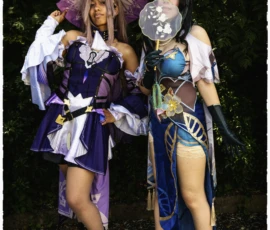 Thierry · 24/05/2026 · 2560 x 3840 Cette photographie met en scène deux personnes déguisées en personnages fantastiques, probablement inspirés d’un jeu vidéo ou d’un anime. Elles portent des costumes colorés et élaborés, avec des éléments comme des capes, des accessoires lumineux et des coiffures stylisées.La composition montre un cadrage serré sur les deux personnages, entourés de végétation. La lumière semble naturelle, avec des ombres douces. Les couleurs dominantes sont les tons violets, bleus et blancs, créant une ambiance à la fois mystique et ludique. Le style est fantastique et théâtral, évoquant un univers de magie et d’aventure.