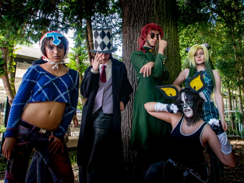 Taunia · 2200 x 1650 Cette photographie met en scène quatre personnes déguisées en personnages de style *anime* ou *cosplay*. Le sujet principal semble être ces cosplayers, posant devant un arbre.La composition est dynamique, avec un cadrage serré sur les personnages. La lumière naturelle, douce et légèrement tamisée, crée des ombres douces. Les couleurs dominantes sont vives : bleu, vert, noir et touches de rouge et jaune.Le style est festif et ludique, évoquant une ambiance convention ou festival de cosplay. L'atmosphère est joyeuse et créative, mettant en valeur les tenues élaborées et les expressions des personnages.