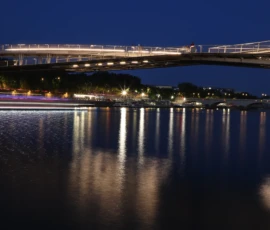 Francoise · 23/05/2026 · 6000 x 4000 Cette photographie met en scène un **pont éclairé** enjambant un plan d’eau calme. Le **sujet principal** est le pont, avec ses structures lumineuses reflétées dans l’eau.La **composition** est équilibrée, avec une symétrie entre les lumières et leurs reflets. Le **cadrage** est large, capturant une vue panoramique nocturne.Les **couleurs dominantes** sont les bleus profonds du ciel et de l’eau, contrastés par les **tons chauds des éclairages** (blancs et jaunes).Le **style** est réaliste et photographique, avec une **ambiance** sereine et presque magique, grâce aux jeux de lumière et aux reflets.