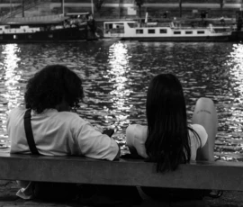Claude · 5573 x 3715 Cette photographie en noir et blanc met en scène deux personnes assises sur un banc face à l’eau. Le sujet principal est leur posture détendue, observant le paysage.La composition est simple et équilibrée, avec une ligne d’horizon bien marquée. Le cadrage serré isole les deux individus, créant une intimité.La lumière douce, probablement crépusculaire, adoucit les contours et reflète sur l’eau. Les couleurs dominantes sont les nuances de gris, renforçant l’atmosphère mélancolique et contemplative.Le style est sobre et réaliste, évoquant une ambiance calme et introspective.