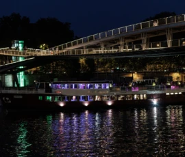 Claude · 5471 x 3647 Cette photographie capture un pont moderne éclairé la nuit surplombant un plan d’eau. Le sujet principal est le pont, avec ses structures métalliques et ses lumières bleutées et blanches.La composition est symétrique, avec des jeux d’ombres et de reflets sur l’eau. Le cadrage est large, incluant aussi des bâtiments en arrière-plan.Les lumières artificielles dominent, créant une ambiance nocturne lumineuse et dynamique. Les couleurs principales sont des teintes froides (bleu, blanc) et des touches de vert.Le style est urbain et contemporain, évoquant une ambiance moderne et paisible.