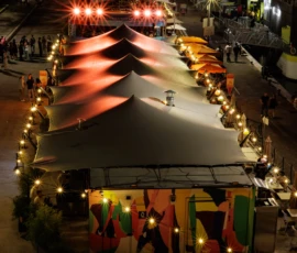 Claude · 3732 x 5598 Cette photographie montre une décoration de Noël stylisée en forme de maison ou de tente, illuminée. Le sujet principal est cette structure festive, ornée de guirlandes lumineuses rouges et de décorations colorées.La composition met en valeur un cadrage serré, centré sur la structure. Les lumières chaudes créent une ambiance chaleureuse et festive. Les couleurs dominantes sont les rouges, blancs et touches de vert et doré. Le style évoque un décor de marché de Noël ou une fête traditionnelle, renforçant une ambiance joyeuse et conviviale.
