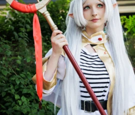 Claude · 3710 x 5565 Cette photographie met en scène une personne déguisée en cosplay, probablement inspirée d’un personnage de manga ou d’anime. Le sujet principal est une jeune femme aux cheveux blancs, vêtue d’une robe blanche et d’un gilet rayé, tenant un bâton magique rouge et or.La composition est centrée sur elle, avec un cadrage serré qui isole le personnage. La lumière naturelle éclaire son visage et ses détails, créant des ombres douces. Les couleurs dominantes sont le blanc, le rouge et les tons pastel, renforçant un style fantastique et élégant. L’ambiance est à la fois mystérieuse et joyeuse, typique des conventions de cosplay.