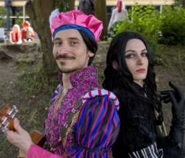 Thibault · 24/05/2026 · 1920 x 1439 Cette photographie met en scène deux personnes déguisées en personnages fantaisistes. Le sujet principal est un homme vêtu d’un costume coloré et extravagant, strié de motifs psychédéliques, avec un turban rose, accompagné d’une femme en tenue sombre et mystérieuse.La composition est serrée, centrée sur les deux personnages. Le cadrage est rapproché, mettant en valeur leurs expressions et leurs tenues. La lumière semble naturelle, avec des ombres douces. Les couleurs dominantes sont vives et contrastées : rose, violet, noir et blanc.L’ambiance est festive et théâtrale, évoquant une fête déguisée ou un événement créatif.