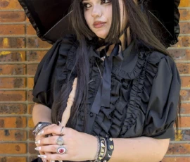 Thibault · 24/05/2026 · 1280 x 1920 Cette photographie met en scène une jeune femme comme sujet principal, vêtue d’une tenue gothique noire : robe à crinoline, collerettes et chapeau. Elle tient un parapluie noir et un accessoire en forme de baguette.La composition est centrée, avec un cadrage serré sur elle, devant un mur en briques. La lumière est naturelle, douce mais contrastée, mettant en valeur les détails sombres de sa tenue. Les couleurs dominantes sont le noir et quelques touches de violet sur ses accessoires.Le style évoque un esthétique gothique ou Lolita, créant une ambiance mystérieuse et élégante.