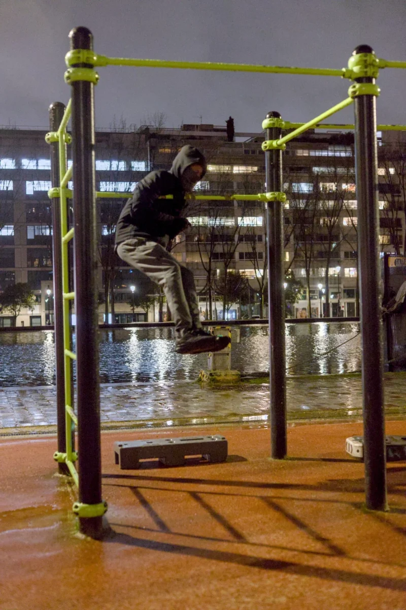 Thibault · 13/02/2026 · 1280 x 1920 Cette photographie capture un skateur en plein saut dans un cadre urbain nocturne. Le sujet principal est le skateur, en mouvement dynamique, encadré par des barrières vertes et noires. La composition est centrée sur l'action, avec un cadrage serré sur la structure et le skatepark.La lumière, tamisée et artificielle, crée une ambiance nocturne, mettant en valeur les contours du skateur. Les couleurs dominantes sont les tons froids (bleu nuit, gris) et les touches de vert des barrières. Le style est réaliste et dynamique, évoquant une ambiance énergique et urbaine.