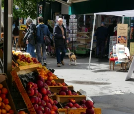 Marine · 16/05/2026 · 4000 x 3000 Cette photographie montre un marché en plein air. Le sujet principal est un étalage de fruits, notamment des pommes et des poires, disposés en crates colorées. La composition inclut des passants et un chien en laisse, ajoutant une touche de vie quotidienne.Le cadrage est large, capturant une scène dynamique. La lumière semble naturelle, probablement celle du jour, avec des ombres douces. Les couleurs dominantes sont les teintes chaudes des fruits (rouge, vert, jaune) et les tons neutres des vêtements et des structures.L’ambiance est conviviale et réaliste, reflétant une scène typique de marché local.