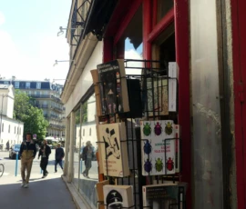 Marine · 16/05/2026 · 4000 x 3000 Cette photographie montre une vitrine de boutique urbaine remplie de boîtes et d’objets divers, probablement des livres ou des produits artisanaux. Le sujet principal est cette vitrine colorée et éclectique.La composition est dynamique, avec un cadrage serré sur la vitrine, encadrée par des éléments architecturaux. La lumière est naturelle et claire, suggérant une journée ensoleillée. Les couleurs dominantes sont vives et variées, avec des tons rouges, verts et blancs.Le style est réaliste et documentaire, capturant une scène de rue typique. L’ambiance est animée et chaleureuse, reflétant une atmosphère urbaine vivante et créative.