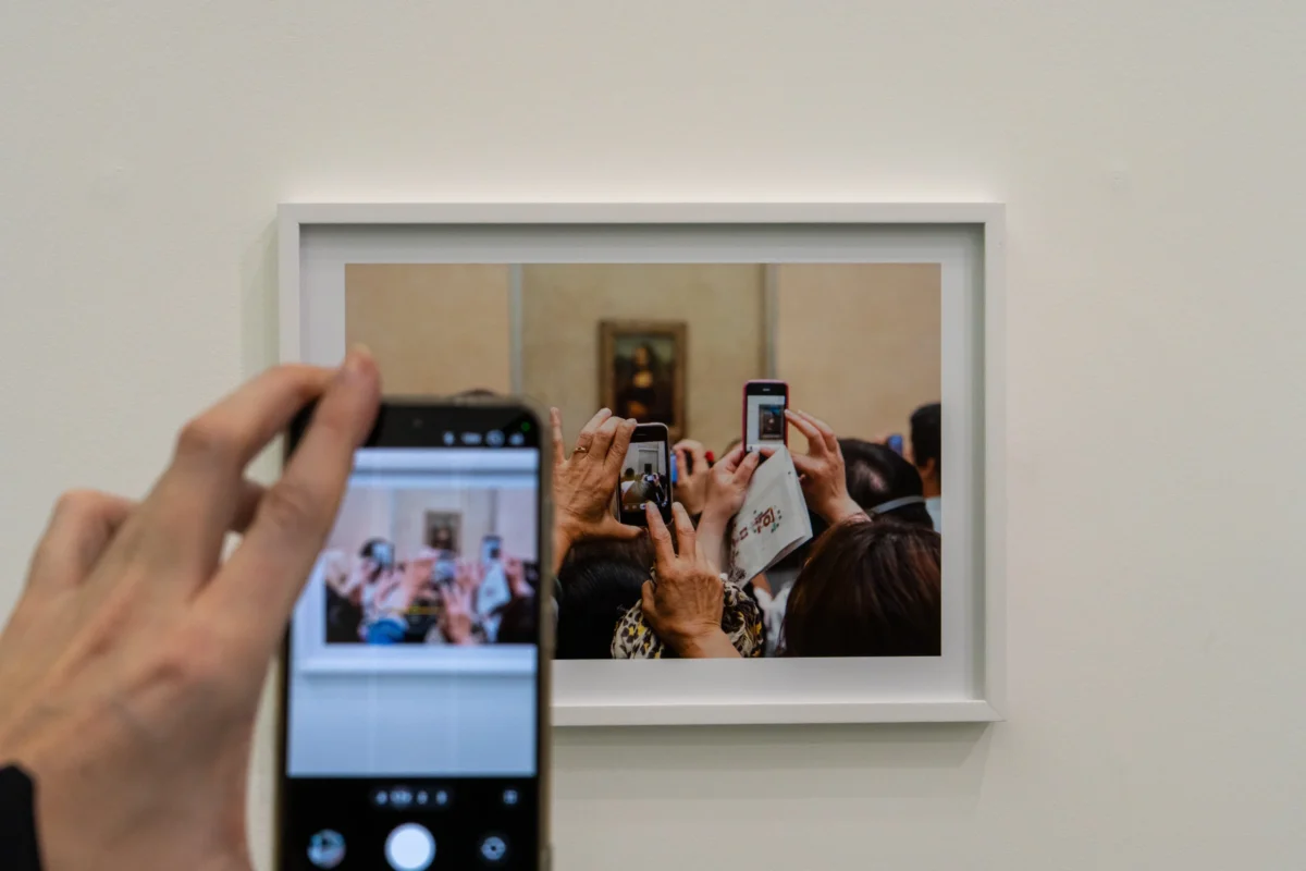 Marc L. · 18/02/2026 · 6946 x 4631 Cette photographie montre une personne prenant en photo, avec son smartphone, une œuvre artistique dans un cadre. Le sujet principal est le reflet de cette scène dans le miroir, révélant plusieurs personnes photographiant l’image.La composition repose sur un jeu de miroir et de répétition, créant une boucle infinie. Le cadrage est serré sur les mains et l’écran du téléphone. La lumière est douce et naturelle, éclairant uniformément la scène. Les couleurs dominantes sont neutres, avec des teintes claires et des reflets froids. L’ambiance est à la fois moderne et artistique, soulignant l’interaction entre l’art et la technologie.