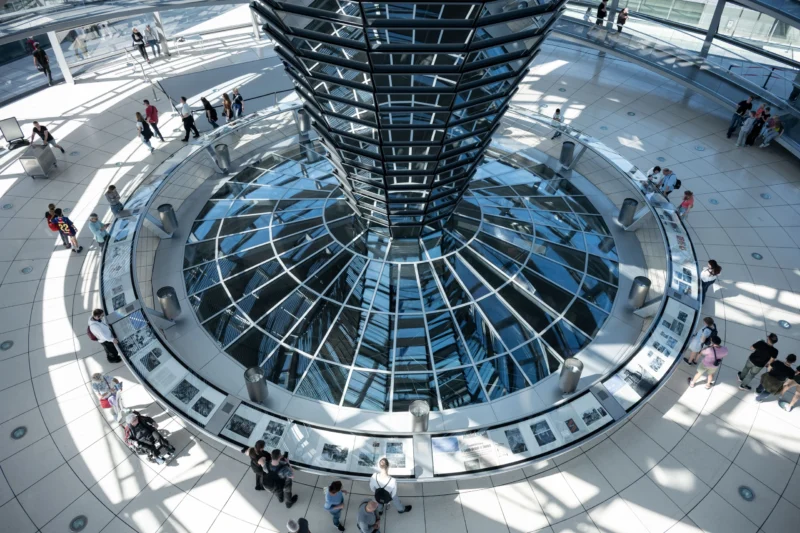 Jean-Marc · 01/05/2026 · 5877 x 3918 Cette photographie montre le **Reichstag de Berlin**, avec son **dôme en verre** comme sujet principal. La composition est axée sur une vue plongeante depuis le centre, révélant les escaliers circulaires et les visiteurs.Le cadrage est large, capturant l’architecture et l’espace. La lumière est naturelle, éclairant généreusement la structure. Les couleurs dominantes sont les **tons froids (bleu, gris)** du verre et de l’acier, contrastant avec les **teintes chaudes** des vêtements des personnes.Le style est **moderne et épuré**, évoquant transparence et démocratie. L’ambiance est **dynamique et ouverte**, mêlant architecture emblématique et fréquentation humaine.