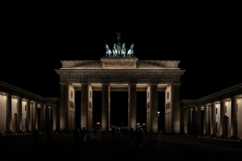 Jean-Marc · 01/05/2026 · 5801 x 3867 Cette photographie montre le **Brandenbourg**, symbole emblématique de Berlin. Le **sujet principal** est l’arc de triomphe éclairé, avec sa quadrige en haut. La **composition** est symétrique, avec des colonnes imposantes encadrant l’entrée.Le **cadrage** est frontal et serré, mettant en valeur la monumentalité du bâtiment. La **lumière** est tamisée, créant un contraste entre les zones éclairées et l’obscurité ambiante. Les **couleurs dominantes** sont des tons chauds (beiges, jaunes) et des noirs profonds.Le **style** est épuré et dramatique, renforçant une **ambiance** solennelle et majestueuse, typique des monuments historiques la nuit.