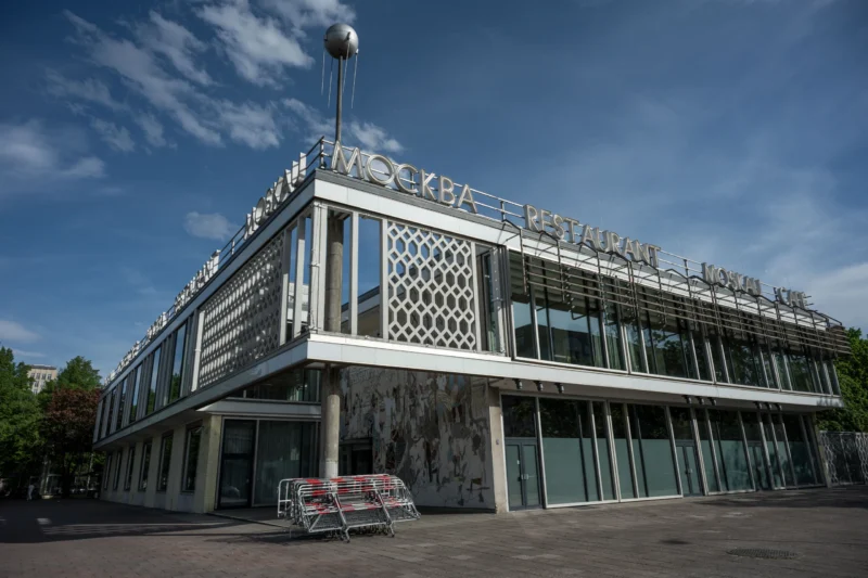 Jean-Marc · 03/05/2026 · 6048 x 4032 Cette photographie montre un bâtiment moderne aux lignes épurées, avec une façade en verre et des motifs géométriques. Le sujet principal est ce bâtiment, marqué par une inscription en lettres blanches sur le toit.La composition est symétrique, avec un cadrage serré sur l’entrée. La lumière est naturelle, douce et légèrement latérale, créant des contrastes sur les surfaces vitrées. Les couleurs dominantes sont le gris, le bleu clair du ciel et les touches de blanc.Le style architectural est contemporain, sobre et fonctionnel. L’ambiance est calme et professionnelle, renforcée par l’absence de foule et le ciel dégagé.