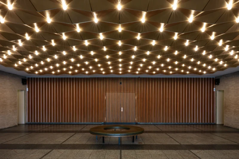 Jean-Marc · 03/05/2026 · 5892 x 3928 Cette photographie montre un espace architectural minimaliste. Le sujet principal est une grande porte en bois aux lames verticales, encadrée par un plafond constellé de petites lumières, évoquant un ciel étoilé. La composition est symétrique, avec un cadrage serré centré sur la porte.La lumière douce et diffuse crée une ambiance chaleureuse et apaisante. Les couleurs dominantes sont les tons bois naturels et les éclats lumineux blancs. Le style est épuré et contemporain, évoquant une atmosphère à la fois moderne et intemporelle, presque sacrée.