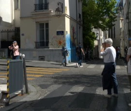 Bao · 5005 x 3094 Cette photographie capture une scène urbaine animée. Le sujet principal semble être un groupe de personnes traversant un passage piéton. La composition montre une rue étroite bordée de bâtiments européens, avec des arbres et des façades colorées.Le cadrage est large, incluant des éléments architecturaux et des passants. La lumière est naturelle et claire, suggérant un jour ensoleillé. Les couleurs dominantes sont les tons neutres des bâtiments, rehaussés par des touches de bleu et de vert.Le style est documentaire, réaliste, reflétant une ambiance quotidienne et paisible dans une ville européenne.