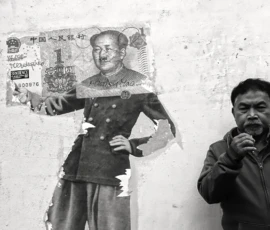 Pierre · 14/05/2026 · 4851 x 2731 Cette photographie en noir et blanc montre un homme debout devant une fresque murale délabrée représentant un personnage historique en uniforme militaire. Le sujet principal est l’homme, vêtu d’une veste matelassée, posant avec un geste théâtral.La composition oppose le visage souriant de l’homme à l’image usée et partiellement effacée du mural. Le cadrage est serré, mettant en valeur les deux figures. La lumière est naturelle, contrastant les ombres et les clartés. L’ambiance est à la fois mélancolique et ironique, renforcée par le style documentaire et le jeu de contrastes entre neuf et ancien.