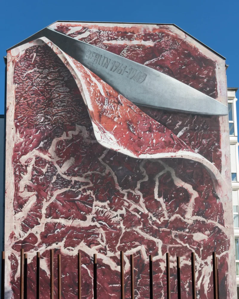 Alice · 30/04/2026 · 3161 x 3951 Cette photographie représente une sculpture ou une œuvre murale stylisée évoquant un steak saignant coupé en deux par un couteau. Le sujet principal est ce steak, avec ses veines et sa texture réaliste.La composition est épurée, centrée sur le steak, avec un couteau en métal argenté. Le cadrage est serré, mettant en valeur les détails. La lumière semble naturelle, éclairant l’œuvre de manière uniforme. Les couleurs dominantes sont les rouges sang et les gris, avec des touches de blanc et d’argent.Le style est réaliste et graphique, évoquant une ambiance à la fois crue et artistique, presque surréaliste.