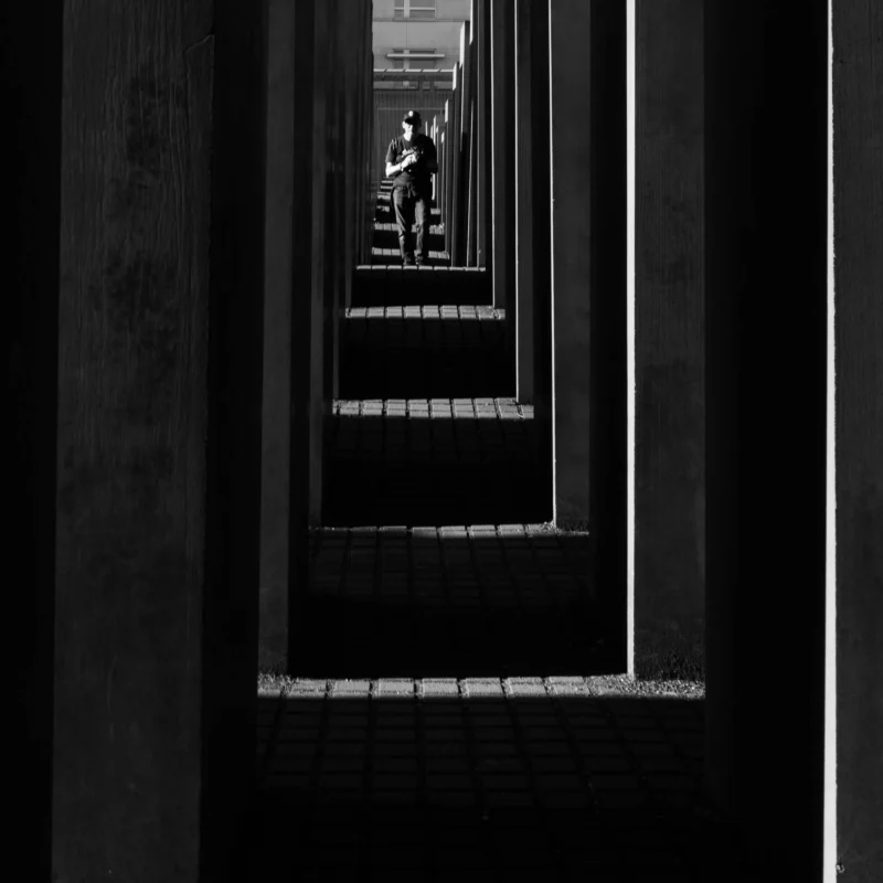 Alice · 01/05/2026 · 3189 x 3189 Cette photographie met en scène un **sujet principal** : une personne en mouvement dans un espace étroit et vertical, probablement un escalier ou un couloir.La **composition** repose sur un **cadrage serré** et des lignes parallèles convergentes, créant une perspective dramatique. La **lumière**, contrastée et naturelle, accentue les ombres et les contours, renforçant l'effet de profondeur.Les **couleurs dominantes** sont les tons de gris, typiques d'une photo en noir et blanc, avec des contrastes marqués.Le **style** est épuré et géométrique, évoquant une ambiance **sombre et mystérieuse**, presque cinématographique. L'atmosphère est à la fois **minimaliste et immersive**.
