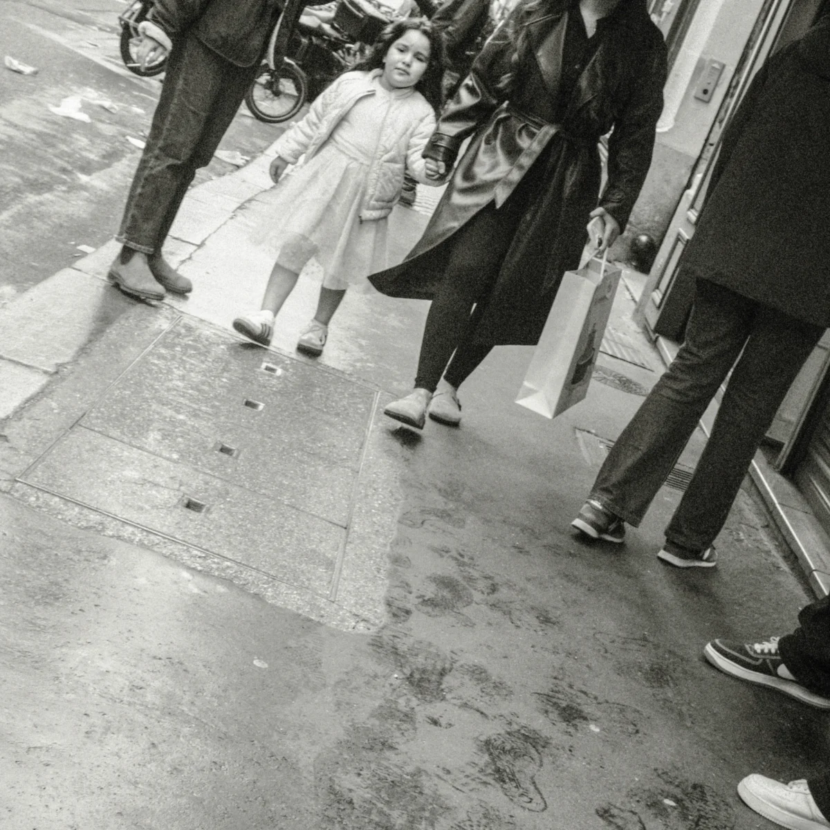 Nathalie F. · 11/04/2026 · 4160 x 4160 Cette photographie en noir et blanc capture une scène urbaine animée. Le sujet principal semble être une femme vêtue d’une veste légère, entourée de passants. La composition met en avant les jambes et pieds des personnes, suggérant un mouvement et une foule.Le cadrage est serré, centré sur les bas des individus, créant une ambiance de vie quotidienne et anonyme. La lumière est naturelle, probablement en journée, avec des contrastes modérés. Les couleurs dominantes sont les nuances de gris, typiques du noir et blanc.Le style est documentaire et spontané, évoquant une ambiance réaliste et authentique de la vie en ville.