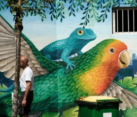 Nathalie F. · 09/05/2026 · 3058 x 3033 Cette photographie montre une fresque murale colorée représentant deux animaux stylisés : un lézard bleu et un perroquet multicolore, posés sur une structure rocheuse. Le sujet principal est cette œuvre artistique, intégrée dans un environnement urbain.La composition est dynamique, avec un cadrage serré sur les animaux. La lumière naturelle éclaire la scène, mettant en valeur les détails. Les couleurs dominantes sont vives : verts, bleus, jaunes et oranges.Le style est réaliste mais avec une touche artistique et fantaisiste. L’ambiance est joyeuse et créative, mêlant nature et urbanité.