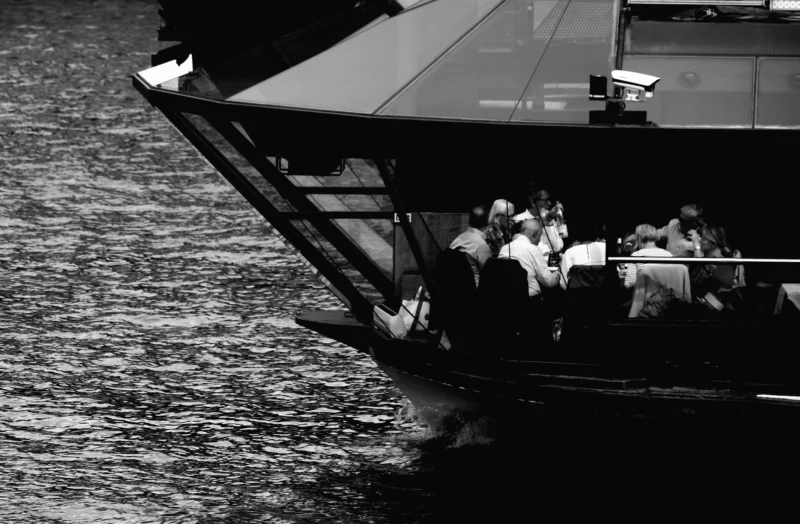 Denis · 13/09/2025 · 4941 x 3237 Cette photographie en noir et blanc met en scène un bateau de plaisance comme sujet principal. La composition montre l’arrière du bateau avec des passagers assis, certains debout, sur la plateforme arrière.Le cadrage est serré, capturant principalement l’eau agitée et une partie du bateau. La lumière, bien que contrastée, crée des ombres marquées, accentuant les détails et les textures. Les couleurs dominantes, bien sûr, sont les nuances de gris, typiques du noir et blanc.Le style est documentaire et spontané, évoquant une ambiance dynamique et légèrement mouvementée, renforcée par les reflets et les éclaboussures sur l’eau.