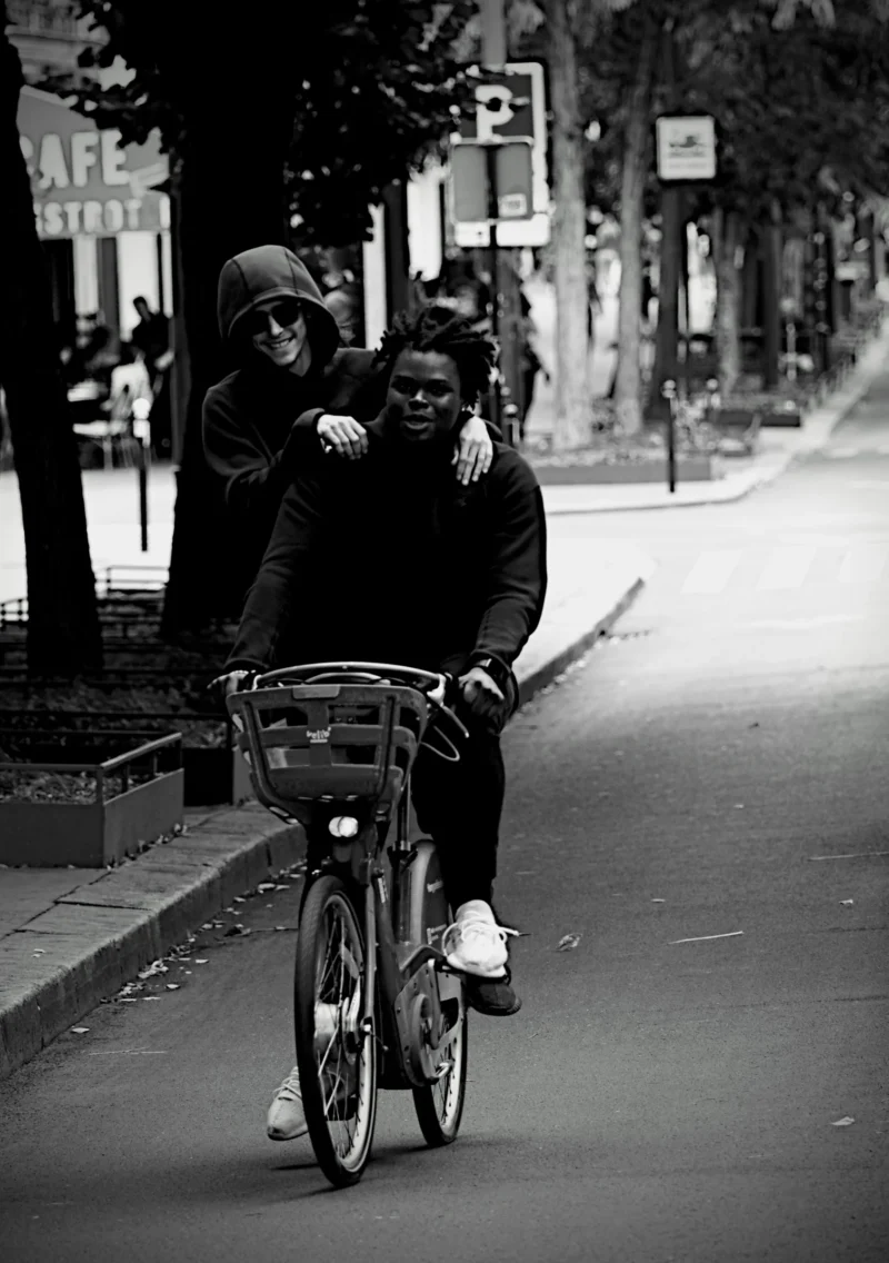 Denis · 13/09/2025 · 3357 x 4766 Cette photographie en noir et blanc met en scène un homme à vélo avec un panier, transportant une personne assise derrière lui. Le sujet principal est ce duo en mouvement.La composition est dynamique, avec un cadrage serré sur les deux personnages. La lumière est naturelle, douce, créant des contrastes modérés. L’ambiance est intime et nostalgique, renforcée par le flou des éléments en arrière-plan.Le style photographique rappelle les clichés vintage, évoquant une époque passée. Les tons gris dominent, accentuant l’aspect rétro et poétique de la scène.