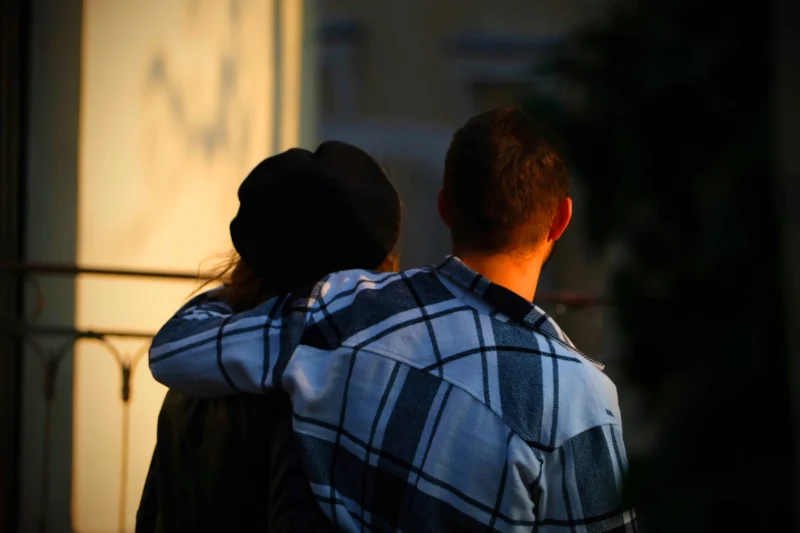 Denis · 21/03/2026 · 4898 x 3265 Cette photographie met en scène deux personnes dos à l'objectif, enlacées. Le sujet principal est leur complicité et leur proximité.La composition est simple et centrée, avec un cadrage serré qui isole les deux silhouettes. La lumière, douce et naturelle, provient probablement du soleil couchant, créant des ombres marquées et une ambiance chaleureuse.Les couleurs dominantes sont les tons chauds (oranges, bruns) et les teintes bleutées du vêtement. Le style est épuré et poétique, évoquant une ambiance intime et émouvante.
