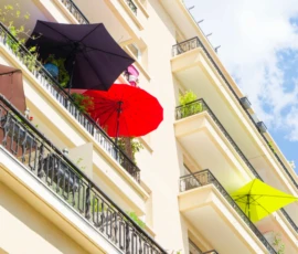 Monique · 09/05/2026 · 6240 x 4160 Cette photographie met en scène des parapluies colorés accrochés à des balcons d’un immeuble. Le sujet principal est ces parapluies, disposés en ligne horizontale.Le cadrage est serré sur les balcons, avec une composition symétrique et dynamique. La lumière est naturelle et éclatante, suggérant un jour ensoleillé. Les couleurs dominantes sont vives : noir, rouge, vert et jaune.Le style est photographique et esthétique, évoquant une touche de joie et d’originalité. L’ambiance est joyeuse et artistique, typique d’un lieu urbain créatif et coloré.